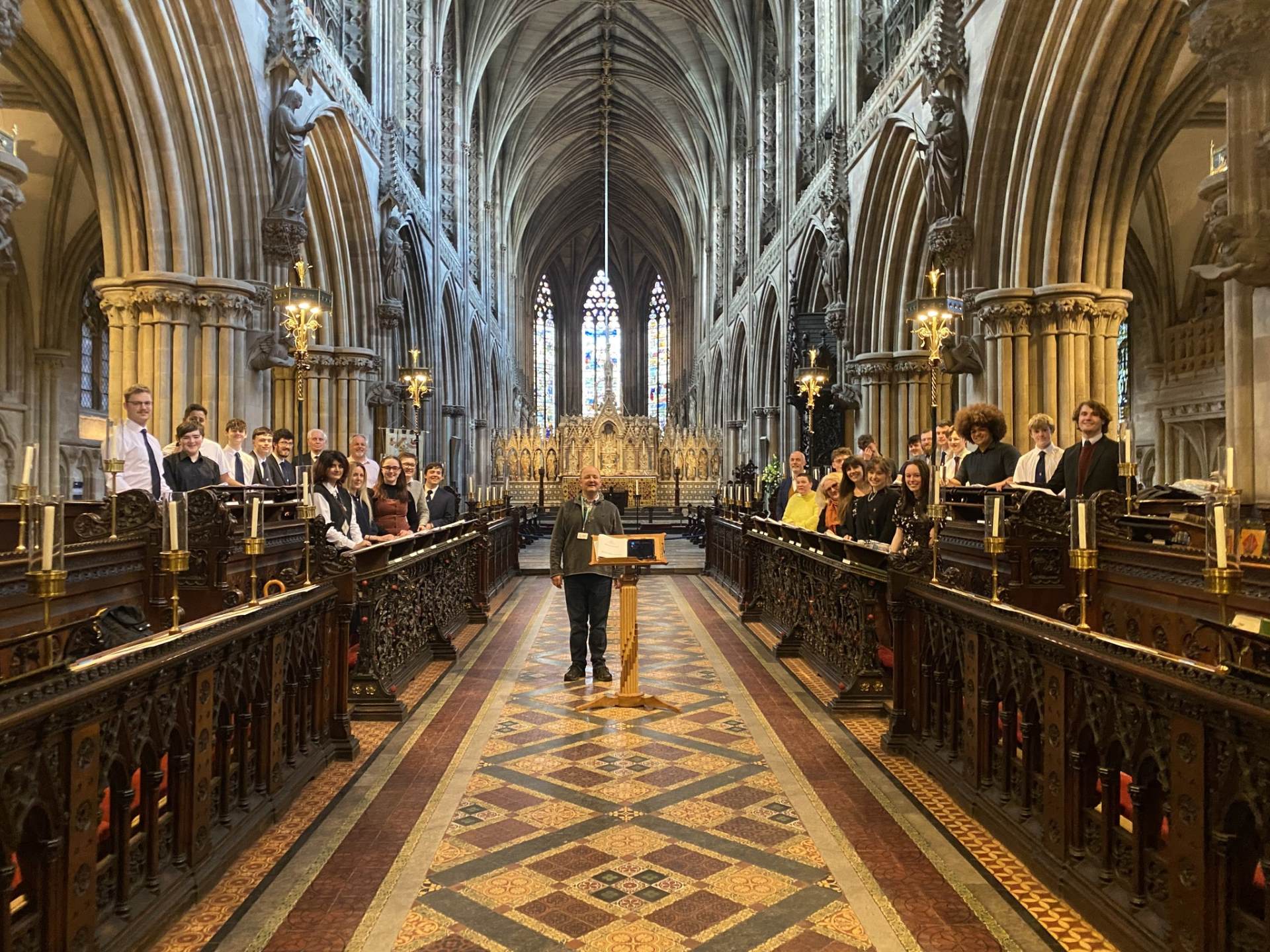 A photo of former choristers in the Quire stalls in Lichfield Cathedral with conductor Ben Lamb
